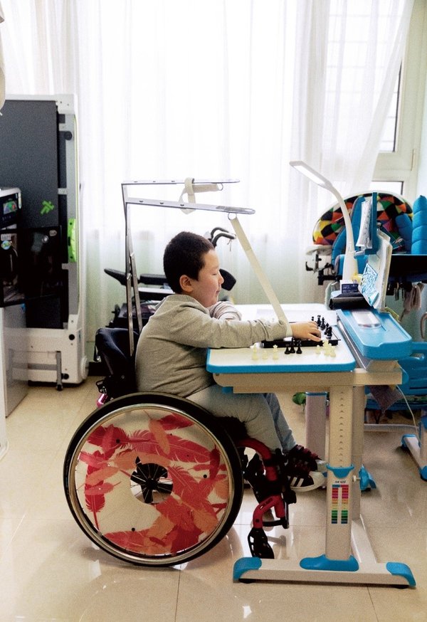 每个周末，草根都会去棋院学习国际象棋，平时在家，也要研究棋谱拆解对局。轮椅上方的松紧带支架，是妈妈根据图纸在淘宝选购材料后亲手制作。使用这个支架，能让草根在下棋时更加轻松舒适。